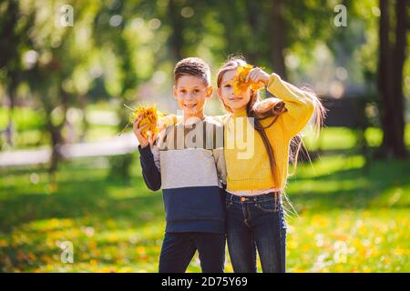 Glückliche Zwillinge Jugendliche Junge und Mädchen posiert umarmt sich im Herbst Park mit gefallenen gelben Blättern in der Hand bei sonnigem Wetter. Herbstthema Stockfoto