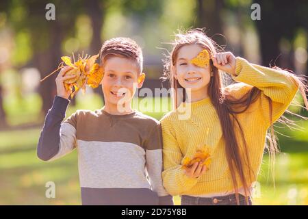 Glückliche Zwillinge Jugendliche Junge und Mädchen posiert umarmt sich im Herbst Park mit gefallenen gelben Blättern in der Hand bei sonnigem Wetter. Herbstthema Stockfoto