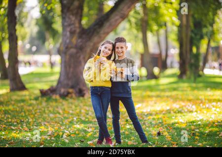 Glückliche Zwillinge Jugendliche Junge und Mädchen posiert umarmt sich im Herbst Park mit gefallenen gelben Blättern in der Hand bei sonnigem Wetter. Herbstthema Stockfoto