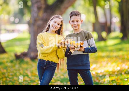Glückliche Zwillinge Jugendliche Junge und Mädchen posiert umarmt sich im Herbst Park mit gefallenen gelben Blättern in der Hand bei sonnigem Wetter. Herbstthema Stockfoto