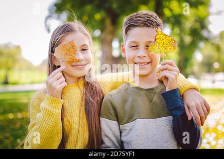 Glückliche Zwillinge Jugendliche Junge und Mädchen posiert umarmt sich im Herbst Park mit gefallenen gelben Blättern in der Hand bei sonnigem Wetter. Herbstthema Stockfoto