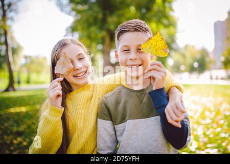 Glückliche Zwillinge Jugendliche Junge und Mädchen posiert umarmt sich im Herbst Park mit gefallenen gelben Blättern in der Hand bei sonnigem Wetter. Herbstthema Stockfoto