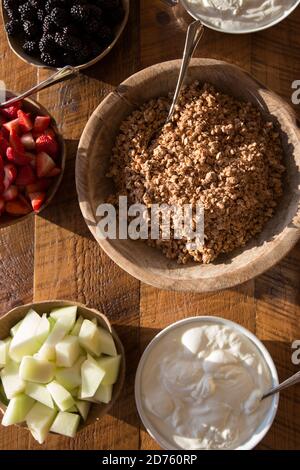 Blick aus der Höhe auf Schalen mit Müsli, Joghurt und frischem Obst auf dem Holztisch Stockfoto