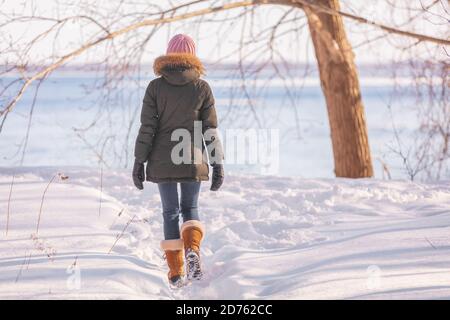 Winter Spaziergang Frau zu Fuß auf Natur Fluss Hintergrund in kalten Outdoor Natur Fluss außerhalb tragen Wollhut, Schal und Pelz Jacke Oberbekleidung Stockfoto