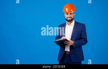 Ein junger Profi trägt einen Hut und trägt einen Zwischenablage auf blauem Hintergrund Stockfoto