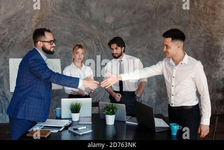 Freut mich, mit Ihnen zu arbeiten Junge moderne Männer in smart Tragen Sie bei der Arbeit im Casual Handshake und Lächeln Kreatives Büro Stockfoto