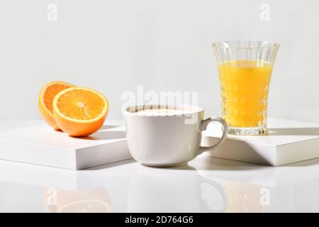 Blick auf eine Tasse frisch zubereiteten Kaffee zwischen einem Orangenschnitt in der Mitte und einem Glas Orangensaft auf einem Tisch auf einem hellen Hintergrund. Obst und Kaffee Konz Stockfoto