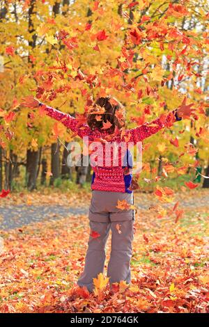 Stehende junge Mädchen genießen fliegende Herbst bunte Blätter in Quebec, Kanada Stockfoto