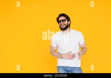 Lachende junge bärtige Mann Kerl in weißen T-Shirt 3d-Brille isoliert auf gelbem Hintergrund. Menschen Lifestyle-Konzept. Film ansehen , Hand auf Stockfoto