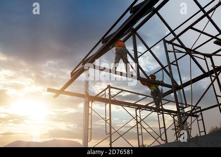 Silhouette des Bauarbeiters auf der Dachkonstruktion auf der Baustelle, Konzept Sicherheitshöhe Ausrüstung. Stockfoto