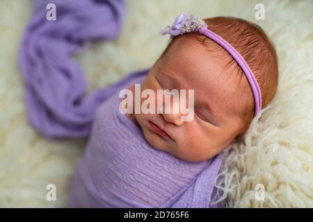 Schlafend, neun Tage altes neugeborenes Baby Mädchen in einem violetten Wrap gewickelt Stockfoto