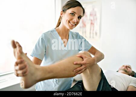 Physiotherapeut, die Behandlung mit dem Patienten in hellen Büro mit Bein Schulung Stockfoto