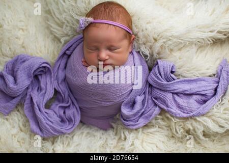 Schlafend, neun Tage altes neugeborenes Baby Mädchen in einem lila Wrap gewickelt. Gedreht im Studio auf violettem Material Stockfoto