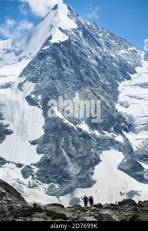 Zinal, Schweiz - 19. Juli 2019: Schöne Aussicht auf schneebedeckten Berg mit Reisenden zu Fuß auf felsigen Weg. Zwei Männer Rucksacktouristen durch Stockfoto