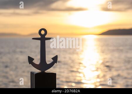 Silhouette des stilisierten Ankers des Schiffes auf der Landung, vor dem Hintergrund des Sonnenuntergangs. Das Konzept der Seefahrt, Abenteuer. Speicherplatz kopieren. Stockfoto