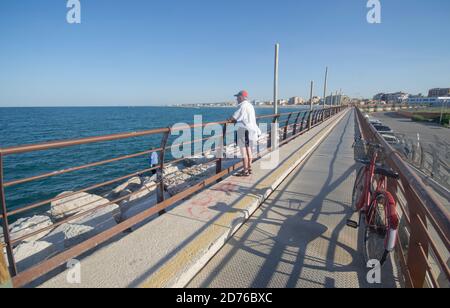 Älterer lokaler Herr hat sein Fahrrad verlassen und beobachtet die seascape und ein Freund Angeln vom Hauptpier von Der Port Stockfoto