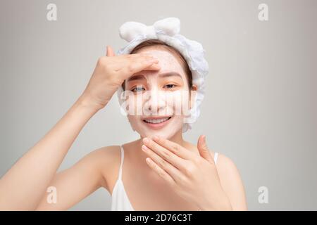 Portrait der selbstbewussten Dame im Bademantel und Handtuch auf dem Kopf Mit Freude, während sie ihr Gesicht mit Tonmaske berühren Mit Anti-Aging-Verfahren Stockfoto