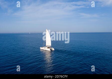 Segeln. Segelboot-Katamaran mit weißen Segeln, bewölktem Himmel und geriffeltem Meereshintergrund. Sommerferien in Ägäis Griechenland Stockfoto