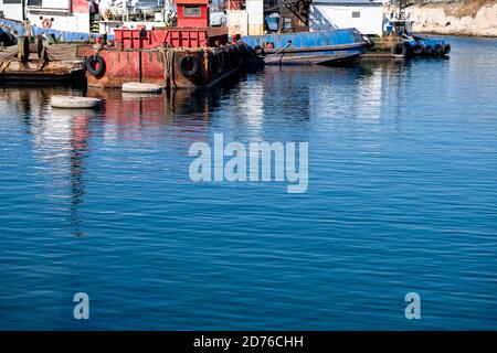 Industrieschiffe und Boote in alten Hafen von Drapetsona Piraeus Griechenland, Reflexion auf dem Meerwasser, sonniger Tag festgemacht. Stockfoto