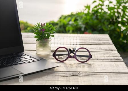 Außenbüro Schreibtisch, Computer-Laptop im Garten, Brille auf dem Tisch, grüne Natur Hintergrund, Quarantäne Home Office-Konzept Stockfoto