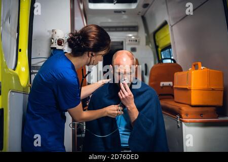 Eine junge Ärztin mit Stethoskop kümmert sich in einem Ambulanzwagen um ihre verletzte Patientin. Stockfoto