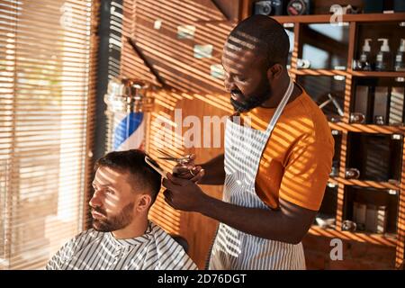 Fröhlicher Barbier Schneiden Client Haar mit Schere im Friseurladen Stockfoto