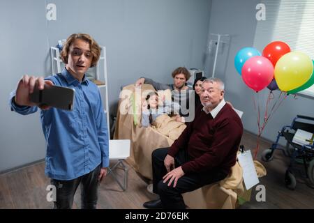 Selfie-Zeit. Ein hübscher junger Junge, der ein Selfie mit seiner Familie auf einer Krankenhausstation macht, besucht die Familie nach einem Unfall ein kleines Mädchen. Stockfoto