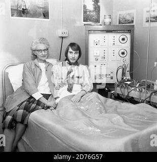 1970, Krankenhaus, ein männlicher Pfleger, der auf einem Krankenhausbett sitzt, mit seiner Technikerin/Krankenschwester, die neben ihm sitzt und seine Hand hält. Er hat eine Dialysebehandlung mit einer Mark 5-Maschine der Cambridge Diaysis-Einheit, Lewisham, Southeast London, England, Großbritannien. Solche Verrat wird verwendet, wenn lebenswichtige Organe des Körpers nicht richtig funktionieren. Hier hat der Mann die Dialyse für seine Nieren, die nicht so arbeiten, wie sie sollten. Die erste erfolgreiche Dialyse fand 1943 statt. Stockfoto