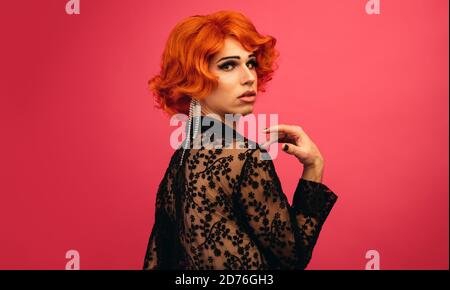 Mann, gekleidet wie eine Frau, die über seine Schulter schaut. Glamarous Drag Queen vor rotem Hintergrund. Stockfoto