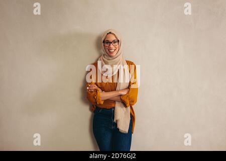 Portriat einer muslimischen Geschäftsfrau stehend mit ihren Amrs gekreuzt. Weibliche Unternehmerin, die sich an eine Wand lehnt. Stockfoto