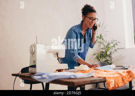 Die Schneiderin erhält zu Hause eine Bestellung von Masken. Frau, die zu Hause arbeitet und am Telefon mit ihrem Kunden spricht. Stockfoto