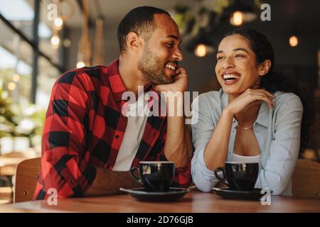 Schönes Paar, das zusammen im Café sitzt und lächelt. Mann und Frau sitzen auf Café-Tablet mit Tassen Kaffee. Stockfoto