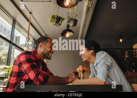 Fröhliches Paar, das im Café sitzt und Hände hält. Mann und Frau sitzen am Restauranttisch und schauen sich an und lächeln. Stockfoto