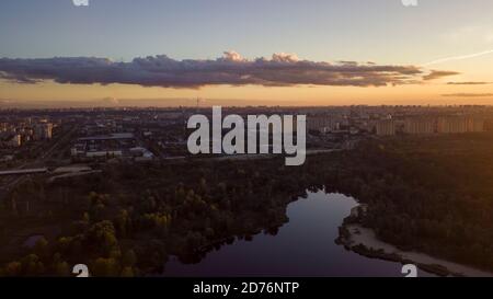Blick auf ein Wohngebiet mit einem See am Rande von Kiew, Ukraine. Herbstansicht aus der Vogelperspektive bei Sonnenuntergang mit Wolken. Stockfoto