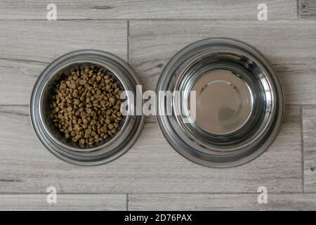 Schüssel mit trockenem Futter und Wasser für Haustiere, Hunde oder Katzen auf grauem Boden Hintergrund. Draufsicht. Stockfoto