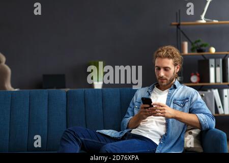 Kurviger Kerl mit Smartphone und lächeln. Glücklicher Mann mit Handy-Apps, SMS-Nachrichten, Surfen im Internet, Blick auf Smartphone, sitzen zu Hause Stockfoto