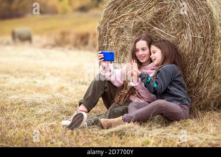 Zwei glückliche Teenager-Mädchen sitzen auf dem Gras auf einer Wiese und machen Selfies mit ihrem Telefon. Stockfoto