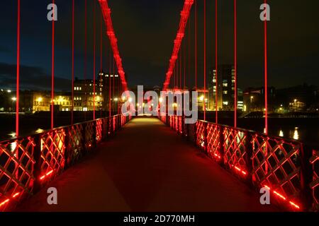 Glasgow, Schottland, Großbritannien... Brücken über den Fluss Clyde bei Nacht. Die South Portland Street Suspension Bridge ist eine Hängebrücke für Fußgänger, die den Fluss Clyde überqueren. Zwischen 1851 und 1853 erbaut, ist es etwa 4 Meter breit und 127 Meter lang und ersetzt die alte Holzbrücke. Es ist eine schöne Möglichkeit, über den Fluss vom südlichen Ende des Stadtzentrums von Glasgow zur Südseite Carlton mit seinem gepflasterten Steinpflaster und georgianischen Reihenhäusern zu gelangen. Stockfoto