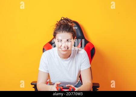 Frau, die hinter einem Spielstuhl in ihren Händen sitzt und rot hält Gamepad auf gelbem Hintergrund Stockfoto