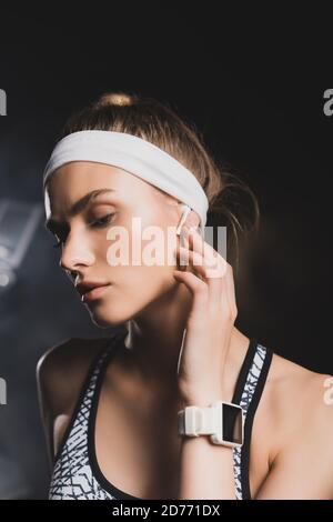 Porträt der Sportlerin mit Smartwatch berühren drahtlose Kopfhörer im Fitnessstudio Stockfoto