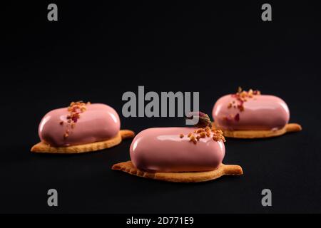 Rosa Kuchen mit Nüssen und trockene Rosenblüte auf schwarzem Hintergrund isoliert dekoriert. Dessert mit glatter Oberfläche, Mousse und Spiegelglasur auf Keks. Leckeres süßes Gericht in der Cafeteria. Stockfoto