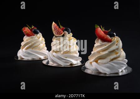 Köstliche Schlagsahne mit Beeren isoliert auf schwarzem Hintergrund. Frische drei Mascarpone Desserts in Reihe mit Feigenscheiben, Erdbeere, Heidelbeere und Himbeere dekoriert. Stockfoto
