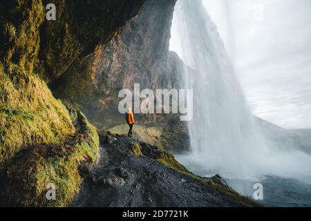Abenteuerlicher Mann unter dem Wasserfall, dem Seljalandsfoss Wasserfall im südlichen Teil Islands Stockfoto