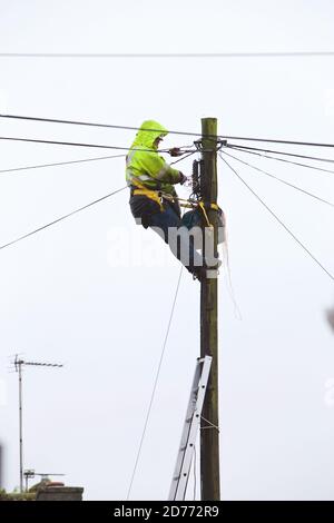 Ein offener Telekommunikationsingenieur bei der Arbeit auf einer Leiter trägt er die richtige PSA für die Arbeit in der Hand und erfüllt gleichzeitig die H&S-Vorschriften. Stockfoto