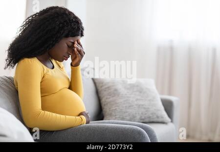 Junge schwangere schwarze Frau, die an Kopfschmerzen oder Migräne leidet Stockfoto