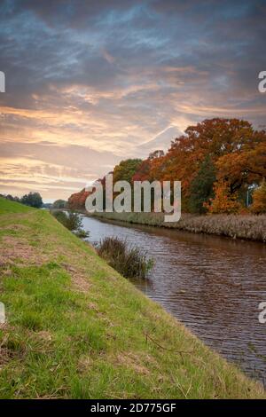 Herbstfarben in den Bäumen entlang des Kanals und einen schönen farbigen Himmel in den Niederlanden, Overijssel Provinz Stockfoto