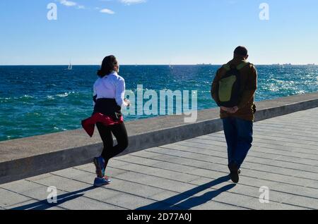 Junge Frau läuft, während ein Mann an einem schönen Tag auf einem Wellenbrecher läuft. Stockfoto