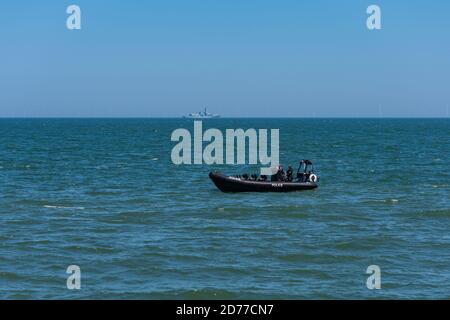 Ein Polizeipatrouillenboot an der Küste der Streitkräfte von Llandudno Tag mit Royal Navy Fregatte HMS Somerset im Hintergrund Stockfoto