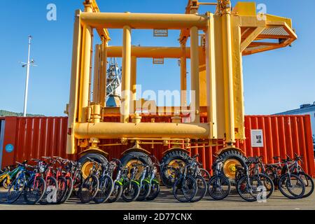 Ein Clark Straddle Carrier zum Bewegen von Containern. Hier mit Leihfahrrädern im Vordergrund. Queens Wharf, Wellington, Neuseeland. Stockfoto