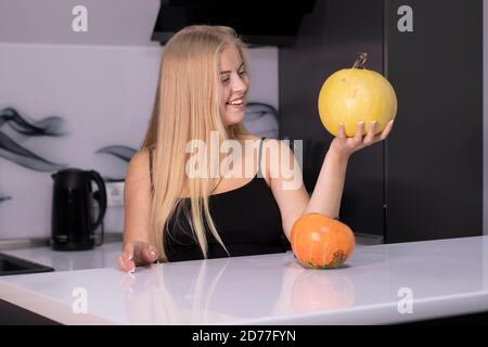 Schöne glückliche Blondine mit zwei Kürbissen in der grauen Küche. halloween-Konzept. Stockfoto
